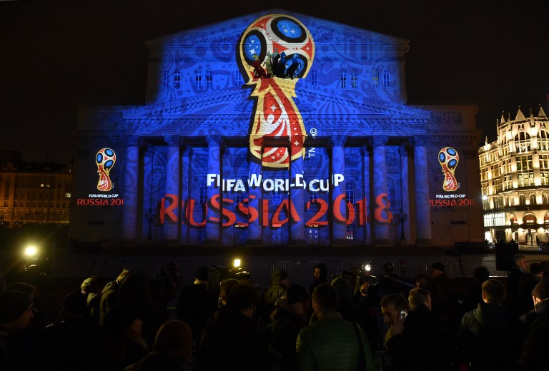 Menschen beobachten, wie die Fassade des historischen Bolschoi-Theaters im Zentrum Moskaus am späten 28. Oktober 2014 mit dem offiziellen Emblem der FIFA Fußball-Weltmeisterschaft 2018 in Russland beleuchtet wird. AFP PHOTO/KIRILL KUDRYAVTSEV